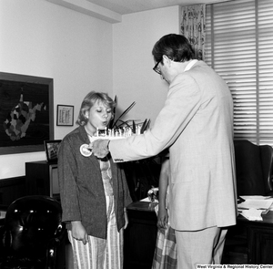 ["Senator John D. (Jay) Rockefeller holds a cake as an unidentified individual from the Presidential Classroom for Young Americans blows out the candles in celebration of West Virginia's birthday."]%