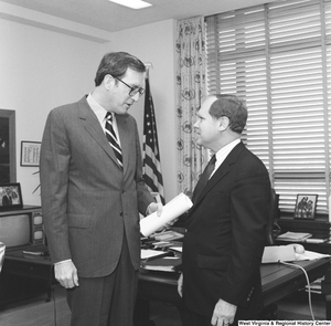 ["With a rolled piece of paper in his hand, Senator John D. (Jay) Rockefeller speaks to an unidentified individual in his office."]%