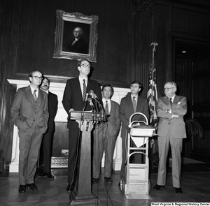 ["Senator John D. (Jay) Rockefeller speaks behind a podium at a press event for the Staggers Rail Reform in a Senate building. Congressmen Nick Rahall and Bob Wise stand behind him with who appear to be Lane Bailey, Rockefeller's State Director, and Tim Gay, Rockefeller's Press Secretary."]%