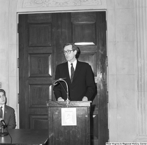 ["Senator John D. (Jay) Rockefeller speaks at an event and stands behind a podium with a \"babies don't come with directions\" poster attached to it."]%