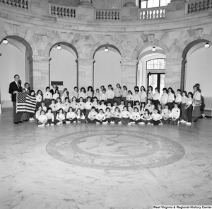 ["Senator John D. (Jay) Rockefeller and Congressman Nick Rahall hold an american flag and pose for a photograph with a large group of young students in a rotunda."]%