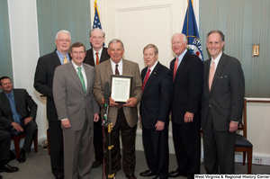 ["A group of Senators hold a framed copy of a Congressional Record."]%