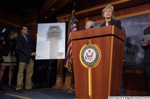 ["Senator Barbara Boxer speaks at a Commerce Committee hearing. Behind her, a staffer holds a poster board with an image of an airport tower."]%