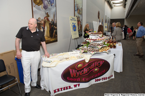 ["A man stands at a table for the Wyckedley Good Cupcakes at an event to celebrate the 150th birthday of West Virginia."]%