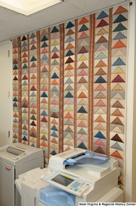 ["A colorful geometric quilt hangs behind a photocopier on a wall in Senator John D. (Jay) Rockefeller's office."]%