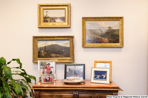 ["Three paintings hang in Senator Rockefeller's office above a table with photographs of some of his family members."]%