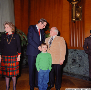 ["A young child wearing green looks into the camera as Senator John D. (Jay) Rockefeller shakes hands with the unidentified man behind him."]%