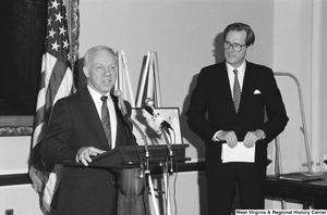 ["Senator John D. (Jay) Rockefeller stands beside another man and watches him speak at a press event."]%
