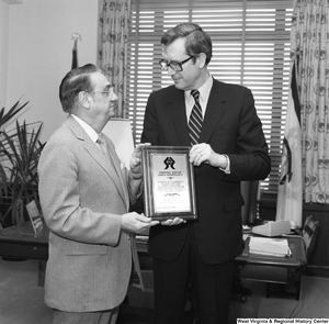 ["Senator John D. (Jay) Rockefeller stands with a member of the Tin Mill Employees Federal Credit Union and holds the award plaque that he has been given. The plaque reads \"Honorable Senator John D. Rockefeller IV: On Behalf of the Members of the Tin Mill Employees Federal Credit Union, We Express our Gratitude and Appreciation for Your Effort, Support, and Services Rendered to the Credit Union Movement. Presented by Nick Battista, President: Michael J. Rinaldo, Sec/Treasurer: Dated February 25, 1986\"."]%