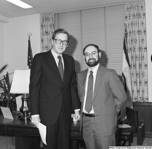 ["Senator John D. (Jay) Rockefeller stands in front of his desk and poses for a photograph with an unidentified individual."]%
