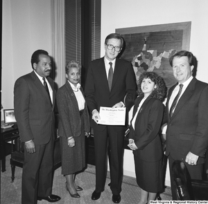 ["Senator John D. (Jay) Rockefeller holds a certificate and stands with several unidentified individuals."]%