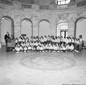 ["Senator John D. (Jay) Rockefeller and Congressman Nick Rahall hold an American flag and pose for a photograph with a large group of young students in a rotunda."]%
