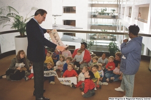 ["Senator John D. (Jay) Rockefeller holds a banner that reads \"Month of the Young Child\" and stands in front of a group of small children in the Hart Building."]%