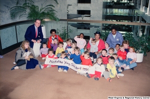 ["Senator John D. (Jay) Rockefeller poses for a photograph with a group of small children in the hallway of the Hart Building. Several children hold a banner that reads \"Month of the Young Child April 1990.\""]%