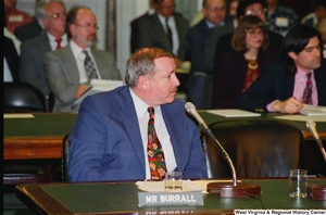 ["A man with a name plaque reading \"Mr. Burrall\" testifies during a Senate hearing."]%
