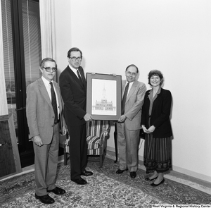 ["Senator John D. (Jay) Rockefeller holds a picture of a church building that has apparently been gifted to him by the three representatives of the West Virginia Humanities Foundation who stand around him."]%