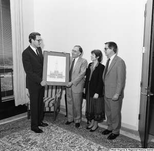 ["Senator John D. (Jay) Rockefeller holds a framed picture of a church building that has presumably been gifted to him by the three representatives of the West Virginia Humanities Foundation who stand next to him."]%