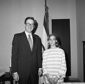 ["Senator John D. (Jay) Rockefeller stands with an unidentified woman in front of the West Virginia state flag."]%