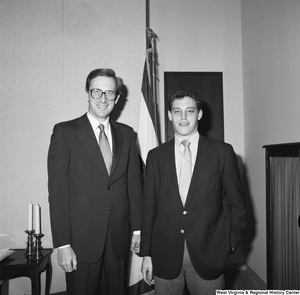 ["Senator John D. (Jay) Rockefeller stands with an unidentified young man in front of the West Virginia state flag."]%