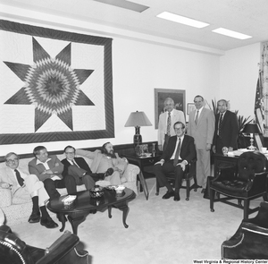 ["Senator John D. (Jay) Rockefeller sits for a photograph and is surrounded by an unidentified group."]%
