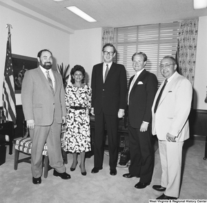 ["Senator John D. (Jay) Rockefeller stands in front of the desk in his office for a photograph with an unidentified group of individuals."]%