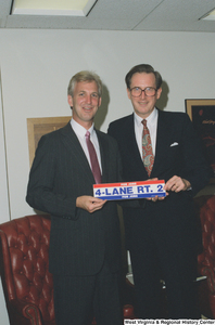 ["Senator John D. (Jay) Rockefeller holds a bumper sticker with a guest in his office. The sticker reads \"For Jobs:  4-Lane Rt. 2\"."]%