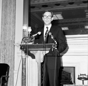 ["Senator John D. (Jay) Rockefeller speaks behind a podium during a press event in a Senate building."]%