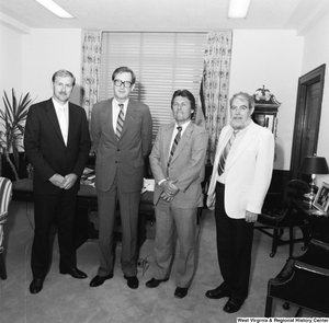 ["Senator John D. (Jay) Rockefeller stands with three unidentified men in front of the desk in his office."]%