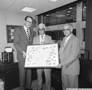 ["Senator John D. (Jay) Rockefeller stands next to two unidentified men and holds a picture of Historic Hinton, West Virginia."]%