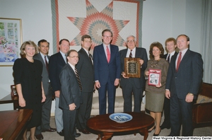 ["Senator John D. (Jay) Rockefeller receives an award from a large group of people in his office. A woman is also holding a copy of \"Physical Therapy Today\" that has a photograph of the Senator on the cover."]%