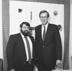 ["Senator John D. (Jay) Rockefeller stands next to an unidentified man in front of the West Virginia quilt hanging on his wall."]%