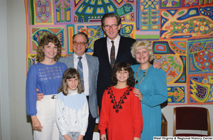 ["Senator John D. (Jay) Rockefeller stands in front of the colorful quilt in his office with a family."]%