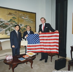 ["Senator John D. (Jay) Rockefeller holds an American flag with two guests in his office."]%