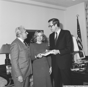 ["Senator John D. (Jay) Rockefeller, his wife Sharon, and author Christopher G. Janus hold a copy of the author's novel, \"Miss 4th of July, Goodbye\". The novel is set in Montgomery, West Virginia and is based on the real-life experiences that Janus's sister had when she immigrated from Greece to West Virginia."]%