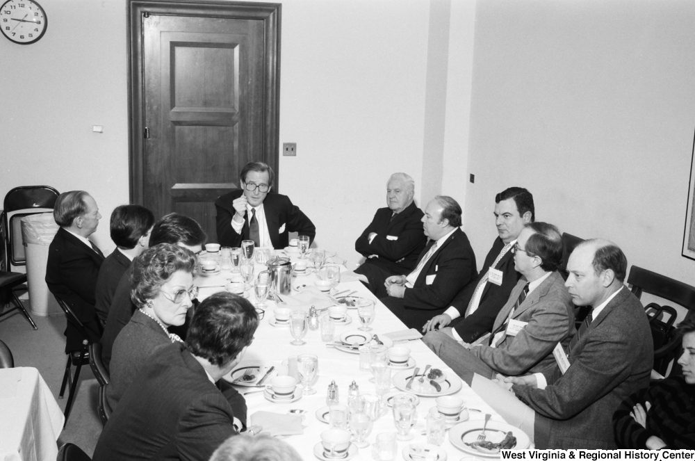 ["Senator John D. (Jay) Rockefeller sits at the head of a table during a breakfast event with numerous unidentified individuals."]%
