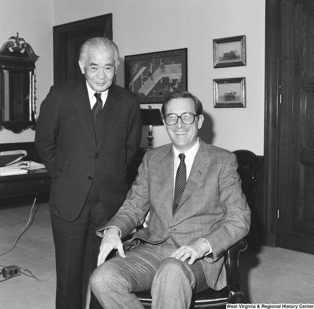 ["An unidentified individual stands beside Senator John D. (Jay) Rockefeller as he sits in a chair."]%