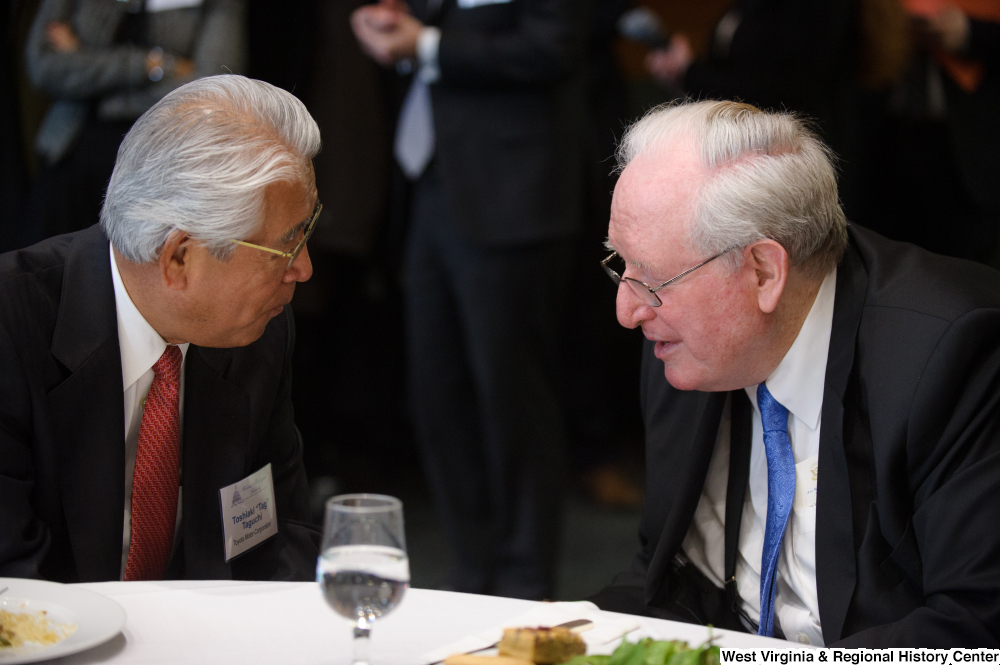 ["Senator John D. (Jay) Rockefeller sits beside a representative of the Toyota Motor Corporation at a luncheon event in Washington."]%