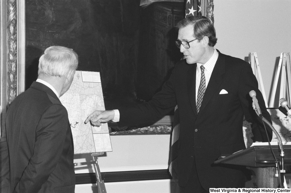 ["Senator John D. (Jay) Rockefeller pointing to a map of West Virginia during a press event."]%