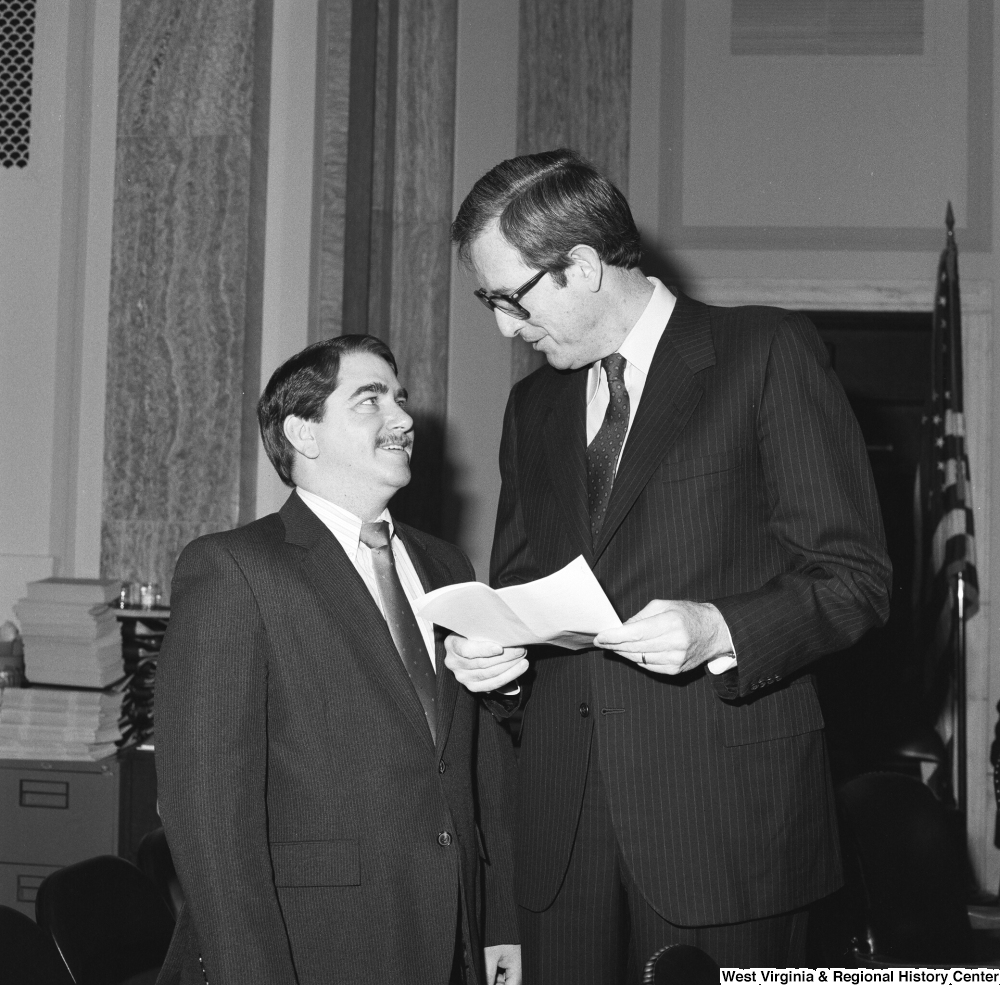 ["Senator John D. (Jay) Rockefeller holds a sheet of paper and talks to an unidentified man in a Senate office."]%
