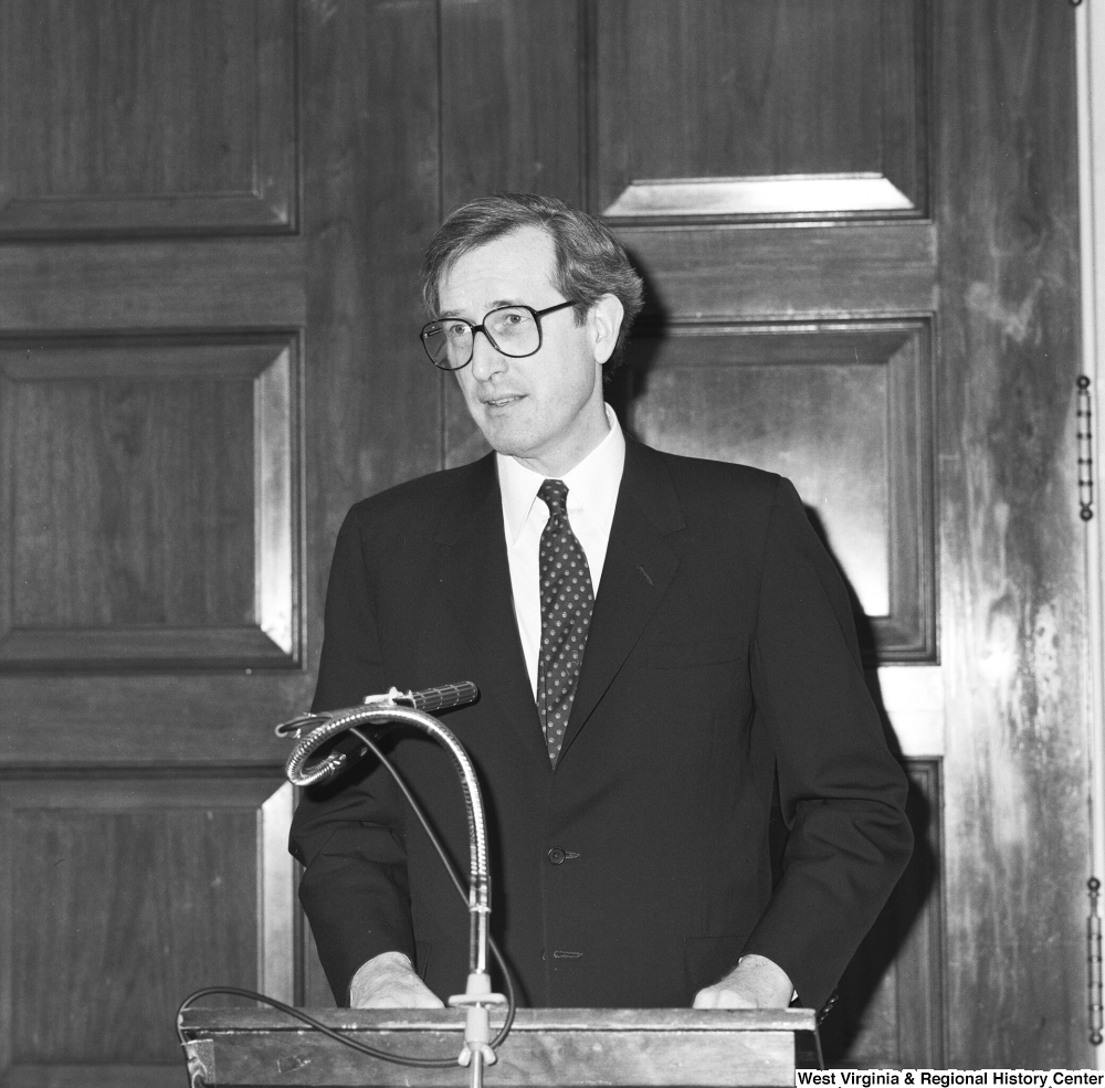 ["Senator John D. (Jay) Rockefeller stands behind a podium and speaks at an unknown event."]%