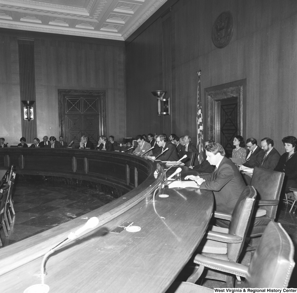 ["This photograph shows Senators sitting around the table at the back of a committee hearing."]%