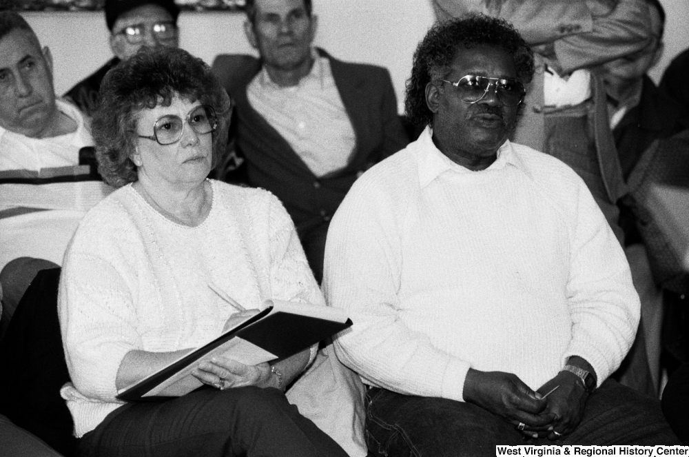 ["A woman sits beside an unidentified man and takes notes during a speech by Senator John D. (Jay) Rockefeller."]%