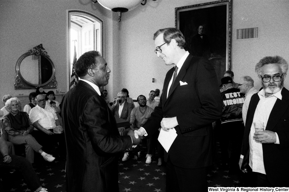 ["Senator John D. (Jay) Rockefeller shakes hands with an unidentified man."]%