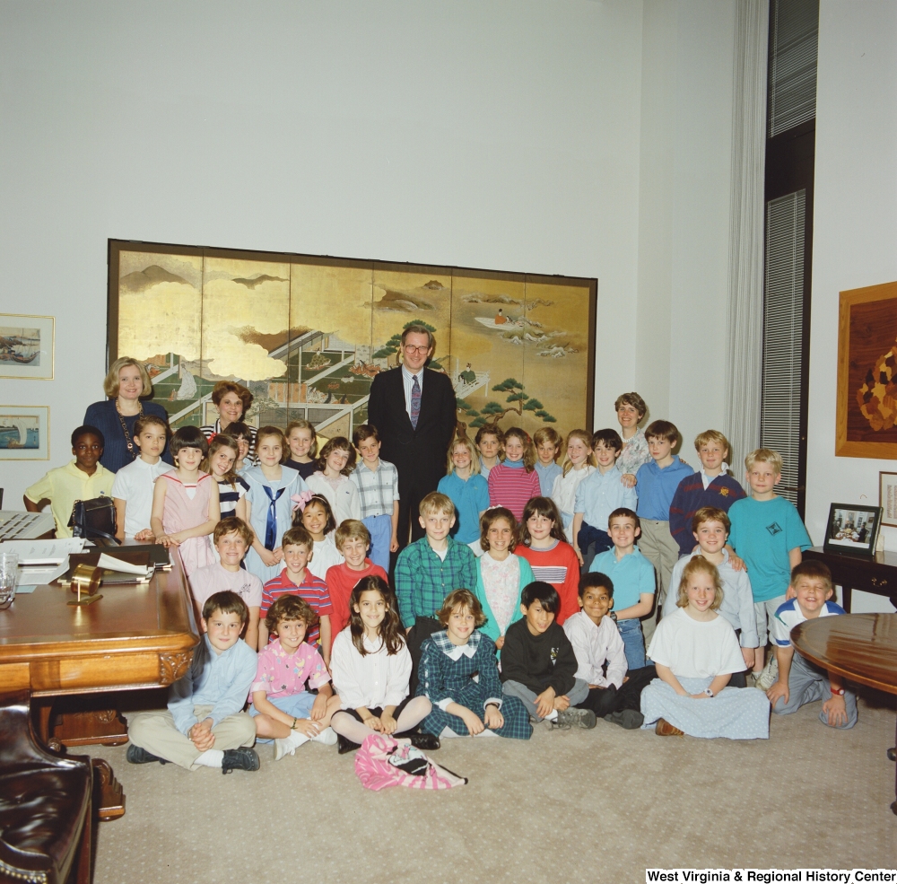 ["Senator John D. (Jay) Rockefeller stands in his office with his wife and a group of young school children."]%