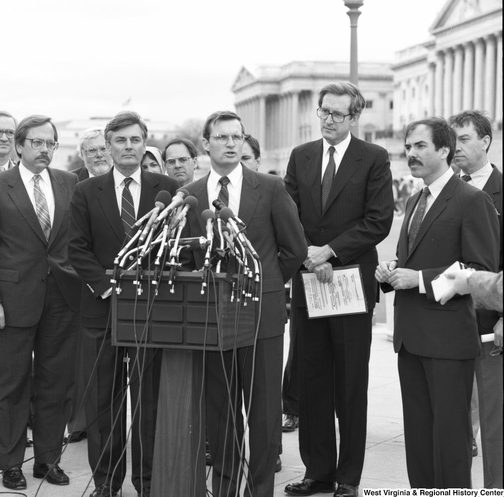 ["Senator John D. (Jay) Rockefeller stands behind a man speaking at an alternative motor fuels event outside the Senate."]%