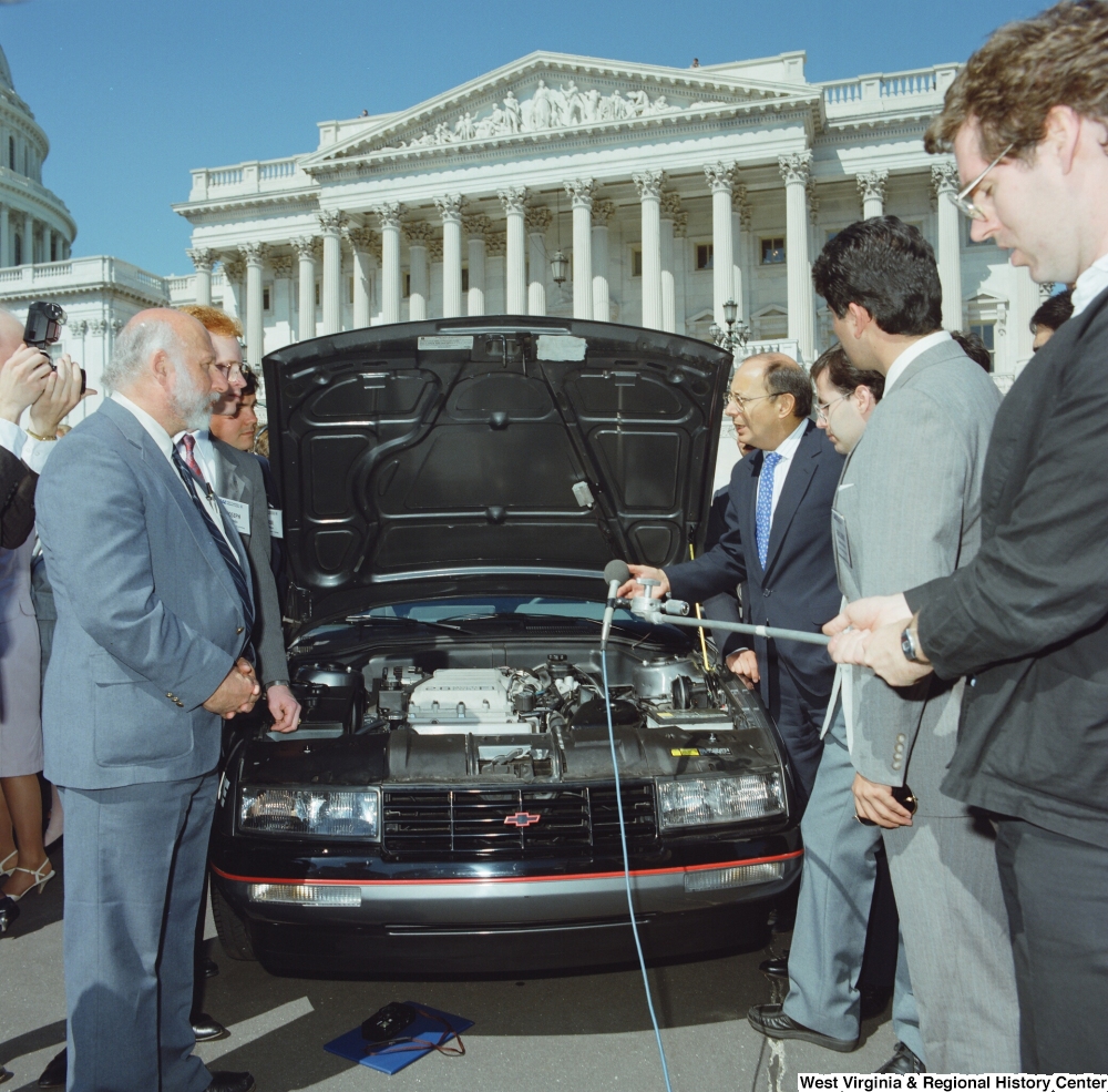 ["Members of West Virginia University's clean energy vehicle team show off their car's engine to a group of people outside the Senate."]%