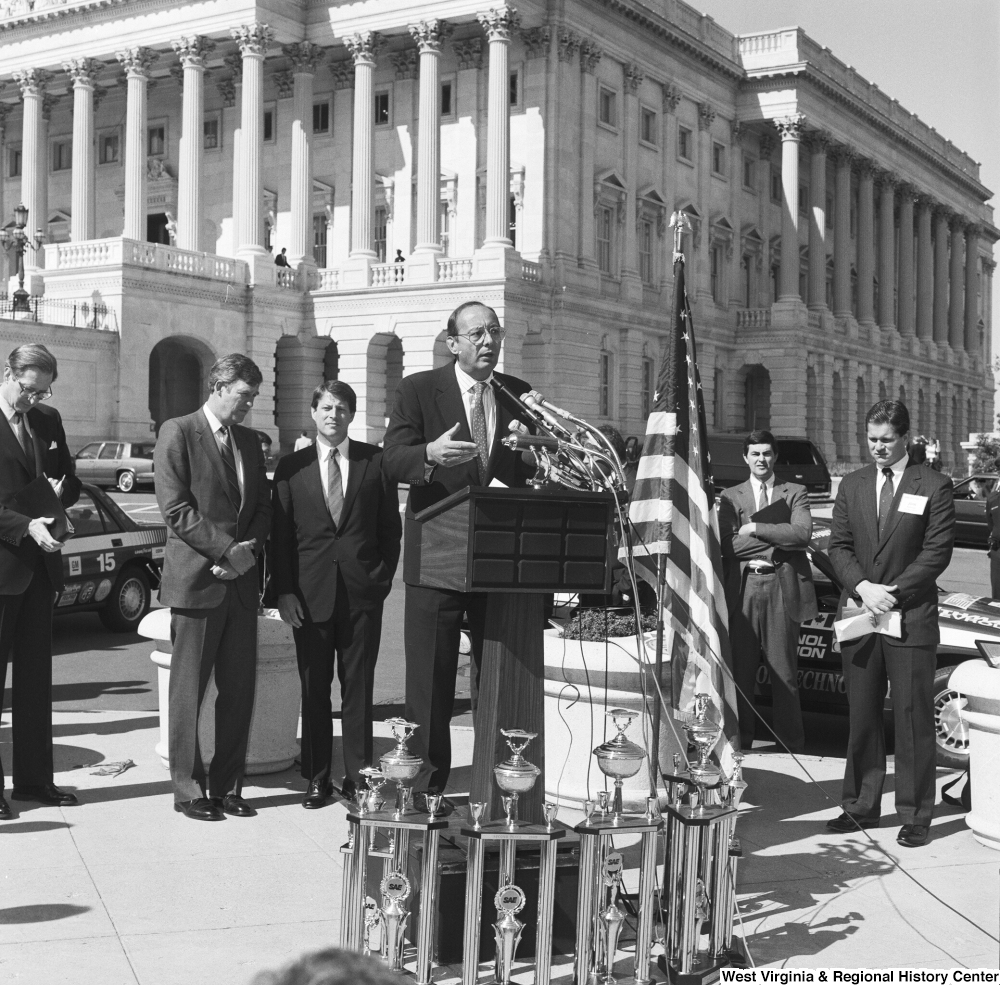 ["Senator John D. (Jay) Rockefeller stands behind as a man speaks at a clean vehicle competition outside the Senate."]%