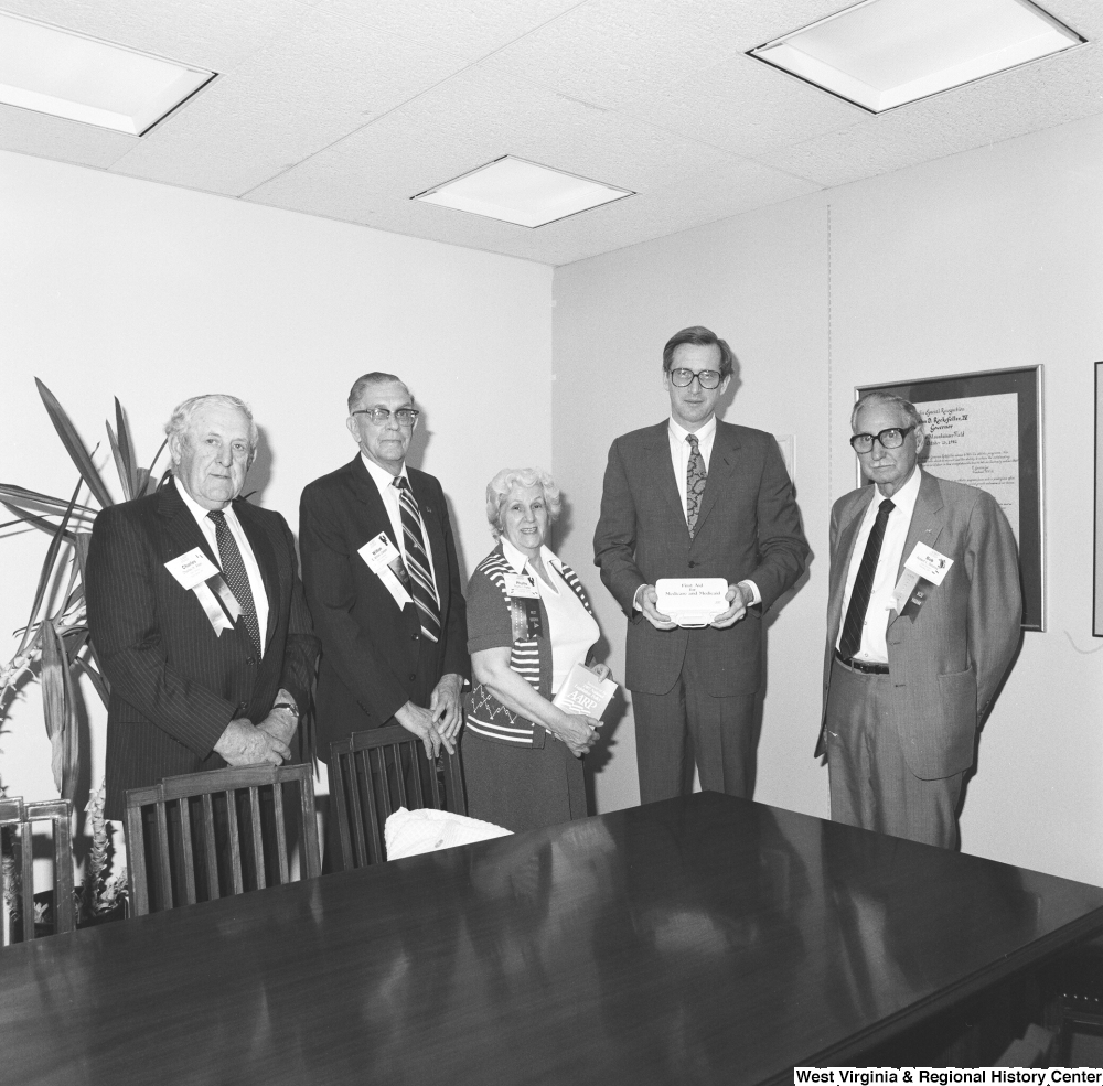 ["Senator John D. (Jay) Rockefeller stands for a photograph with four representatives of the American Association of Retired Persons. The Senator holds a box that reads \"First Aid for Medicare and Medicaid\"."]%