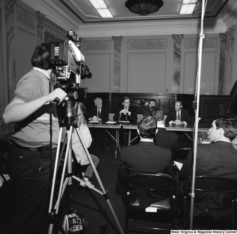 ["A film crew captures a press event where Senator John D. (Jay) Rockefeller and several other men speak."]%