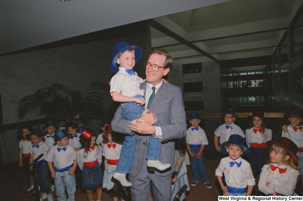 ["Senator John D. (Jay) Rockefeller holds a small boy after he sings in the Hart Building."]%